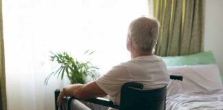 older man in a wheelchair looking out a bright window