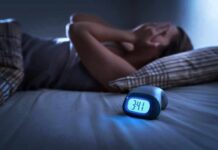 Body Clock Rhythm Linked to Dementia Risk Person lying awake in bed beside a glowing digital alarm clock