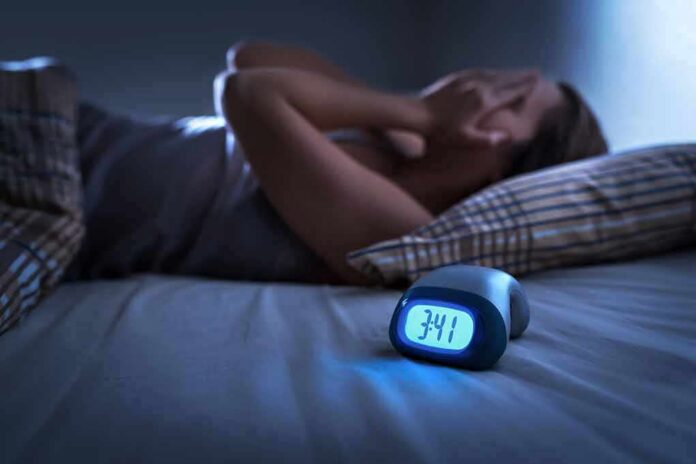 1783889961423-kzp0to-shutterstock-1299304069 Person lying awake in bed beside a glowing digital alarm clock
