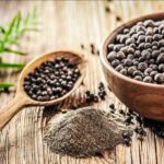 Black peppercorns in a wooden bowl and spoon with ground pepper