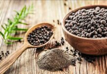 Black peppercorns in a wooden bowl and spoon with ground pepper