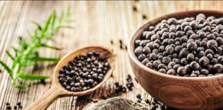 Black peppercorns in a wooden bowl and spoon with ground pepper