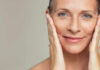 Close-up portrait of a smiling woman gently holding her face