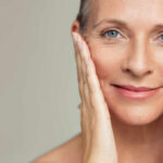 Close-up portrait of a smiling woman gently holding her face