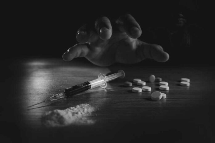 Stop,Drug,Addiction,Concept,International,Day,Against,Drug,Syringe,And A hand reaching for pills next to a syringe and powder on a table