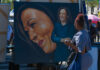A woman admires a large portrait of a smiling female figure at an outdoor event