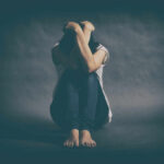 Why Depression Is More Prevalent Among Women A person sitting on the floor with their arms wrapped around their knees, conveying a sense of distress