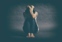 Why Depression Is More Prevalent Among Women A person sitting on the floor with their arms wrapped around their knees, conveying a sense of distress