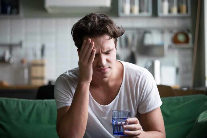 shutterstock_1095874334 Man with headache holding a glass of water