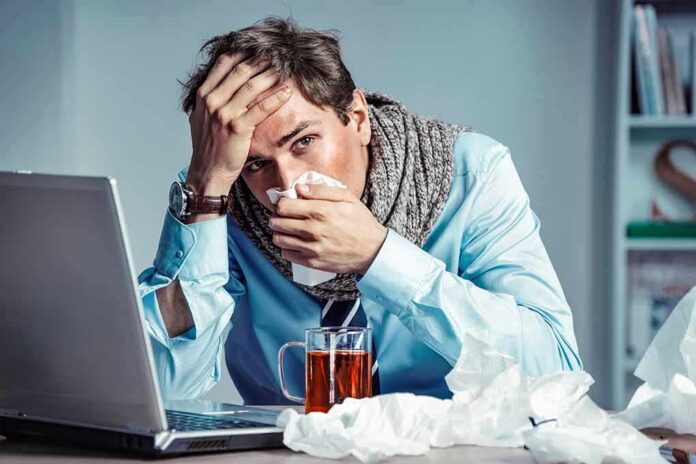 Sick man at desk blowing his nose