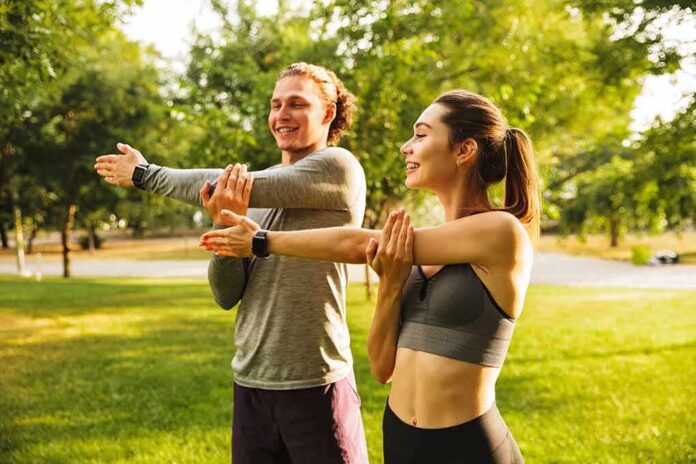 Two people stretching arms in a sunny park