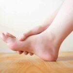 Common mistake that makes aging joints hurt more Hand holding the arch of a bare foot on a wooden floor