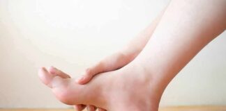 Hand holding the arch of a bare foot on a wooden floor