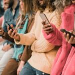 group of people using smartphones while standing in a row