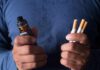 Hands holding a vape device and cigarettes