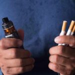 Hands holding a vape device and cigarettes