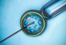 IVF: Fertility Factories Or Family Lifeline? Close-up of a needle and vial with liquid droplets on a blue background