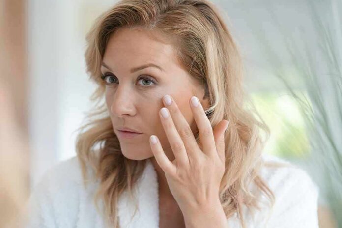 woman touching her cheek while looking in a mirror