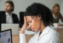 CDC Flags Troubling Fatigue Epidemic Woman in office holding her head with eyes closed