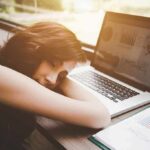 Fasting: Brain Rewire—Or Risk? Woman resting her head on desk beside an open laptop