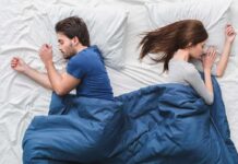 How Your Partner’s Sleep Affects You More Than You Realize Couple sleeping back to back in bed under blue blanket