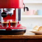 Red espresso machine brewing two shots beside croissants on a plate