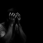 Person holding head in hands in dark lighting