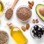 Plant-Based Trap: Snacks That Fool the Heart Assorted healthy fats with avocados, nuts, seeds, olives, and oils on a white background