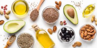 Assorted healthy fats with avocados, nuts, seeds, olives, and oils on a white background
