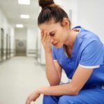 Nurse in blue scrubs sitting with head in hand