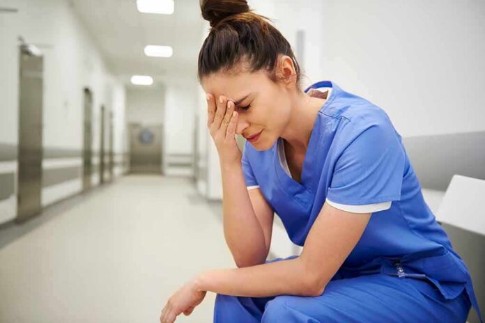 Nurse in blue scrubs sitting with head in hand