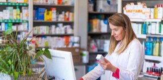 Pharmacist checking medication box at computer counter