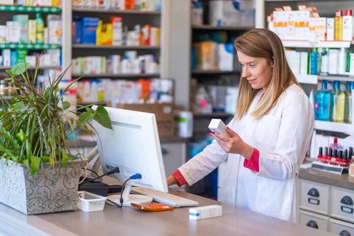 Pharmacist checking medication box at computer counter