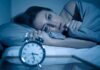 How Nighttime Light Exposure Reshapes Your Heart Woman lying awake in bed beside an alarm clock