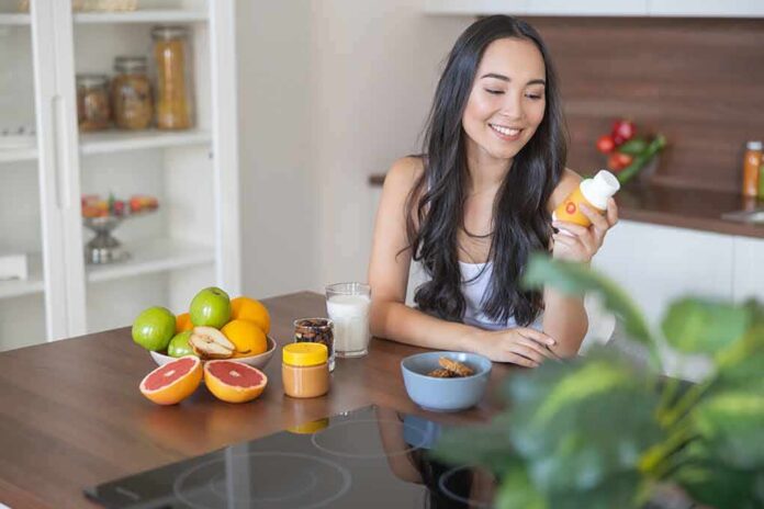 Woman sitting at kitchen counter holding a supplement bottle