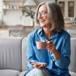 Dementia Care: Practical Tips For Families In The Early Stages Smiling older woman with gray hair holding a pink coffee cup on a sofa