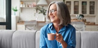 Smiling older woman with gray hair holding a pink coffee cup on a sofa