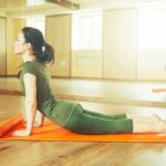 Pain-Free Knees From Butt Squeezes? Woman practicing yoga on an orange mat in a bright studio
