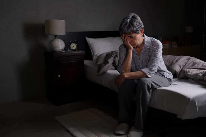 Older adult sitting on bed with head in hand