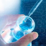 Hand holding vial as pipette adds blue liquid