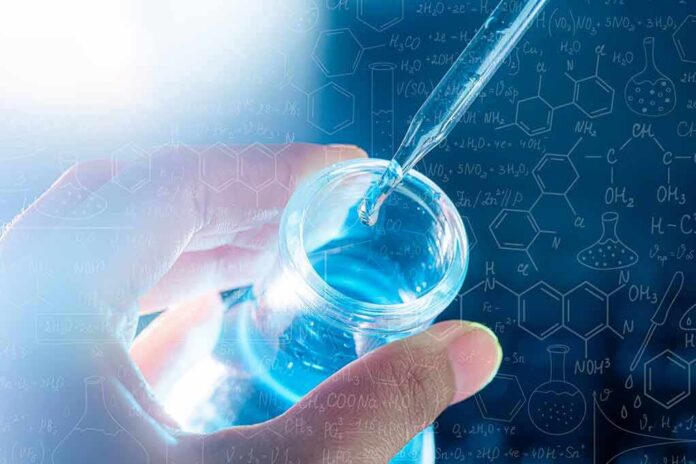 shutterstock_1923908270 Hand holding vial as pipette adds blue liquid