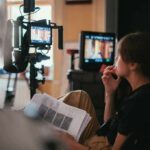 film crew member reviewing script beside monitors on set