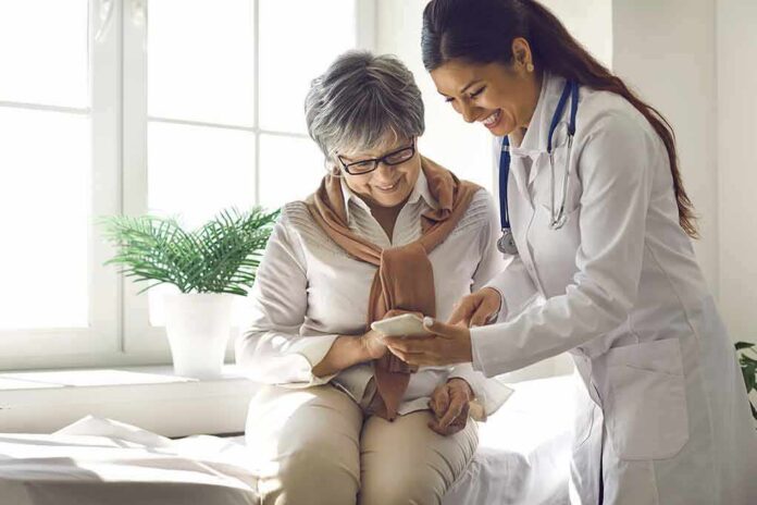 shutterstock_1968439885 Doctor shows smartphone to smiling older woman in clinic