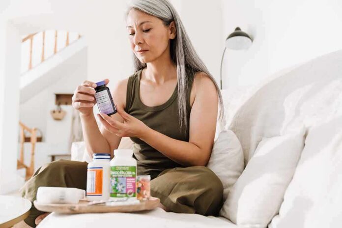 shutterstock_2061961277 Woman reading supplement bottle label on a sofa