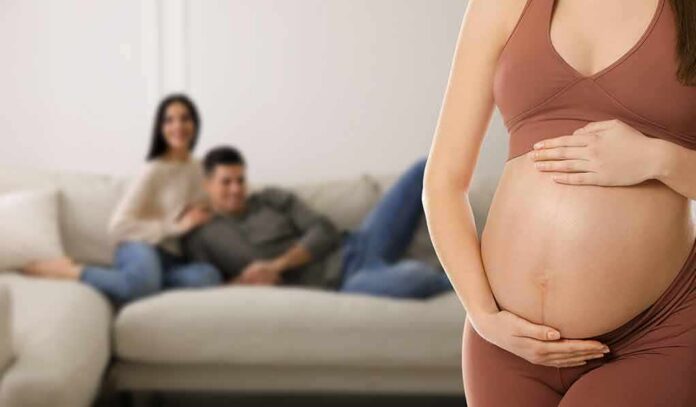 shutterstock_2150484801 Pregnant woman holding her belly in a living room