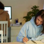 Off-the-Charts Mental Health Numbers Among Gen Z Student in blue hoodie writing in notebook at desk