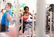 Woman lunging on sled in gym next to man using cable machine