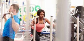 Woman lunging on sled in gym next to man using cable machine