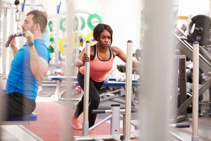 shutterstock_296936102 Woman lunging on sled in gym next to man using cable machine