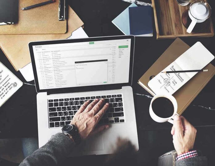 shutterstock_349534082 Person working on a laptop with email inbox open and holding a cup of coffee